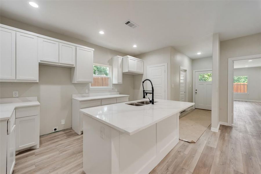 Kitchen with sink, white cabinets, light wood-type flooring, and a kitchen island with sink