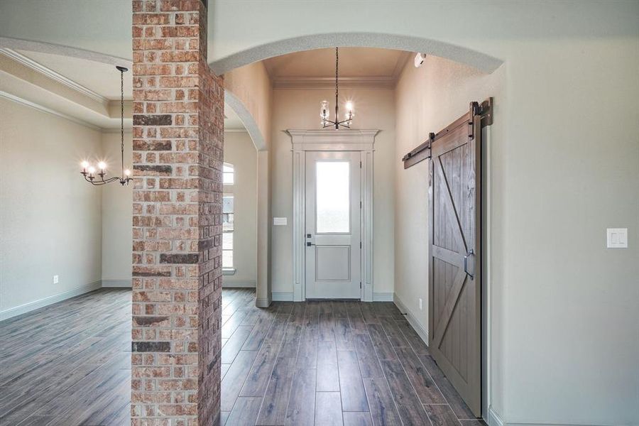 Foyer entrance featuring a notable chandelier, crown molding, brick wall, a barn door, and dark wood-type flooring