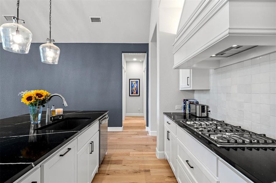 Kitchen featuring white cabinetry, light wood-type flooring, premium range hood, backsplash, and sink