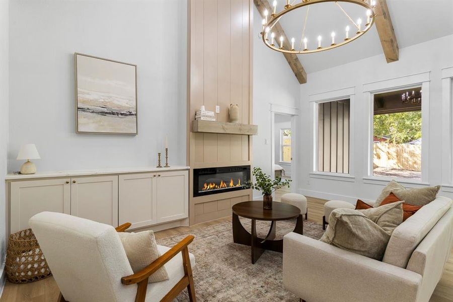 Living room featuring beam ceiling, light hardwood / wood-style flooring, a large fireplace, an inviting chandelier, and high vaulted ceiling