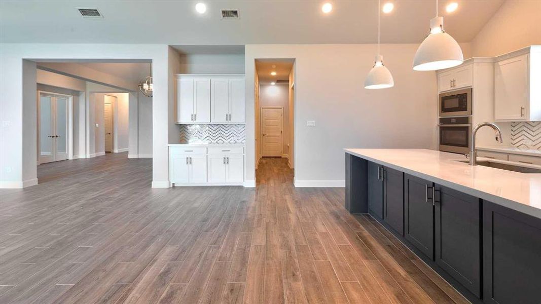 Kitchen with white cabinetry, tasteful backsplash, hardwood / wood-style flooring, sink, and black microwave