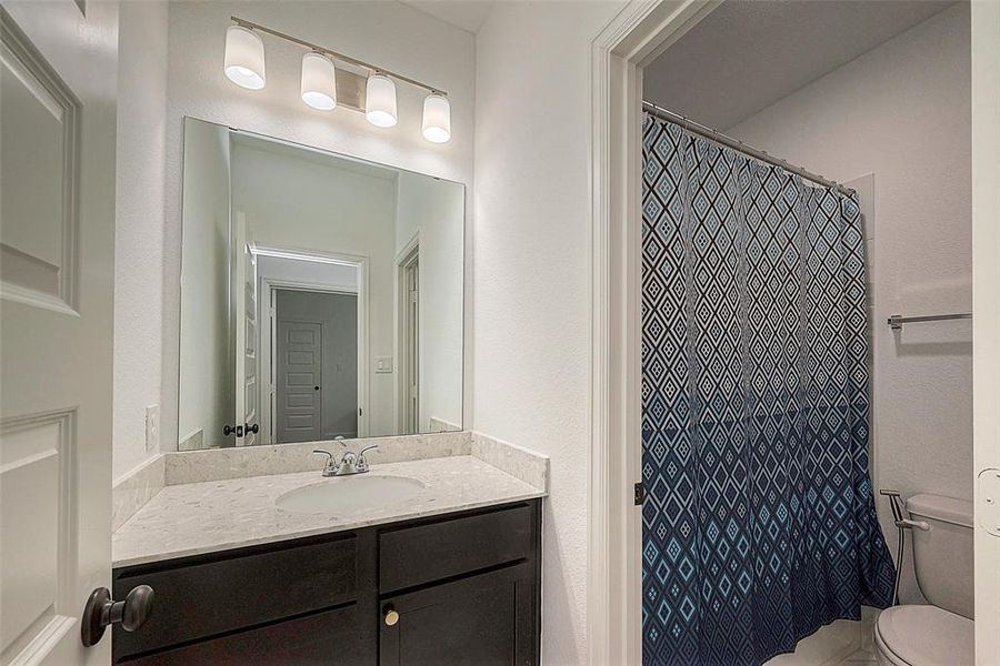 This is a modern bathroom featuring a large mirror with overhead lighting, a single sink vanity with ample countertop space and storage, and a full bathtub with a decorative shower curtain. The room has a clean, neutral color scheme.