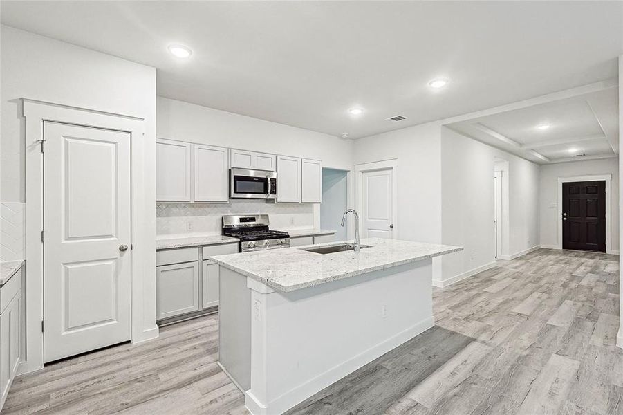 Kitchen featuring light wood-type flooring, stainless steel appliances, sink, decorative backsplash, and a center island with sink