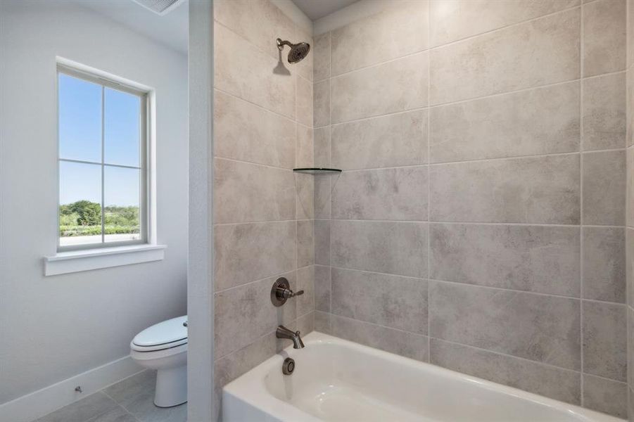 Bathroom with toilet, a healthy amount of sunlight, tile patterned floors, and tiled shower / bath