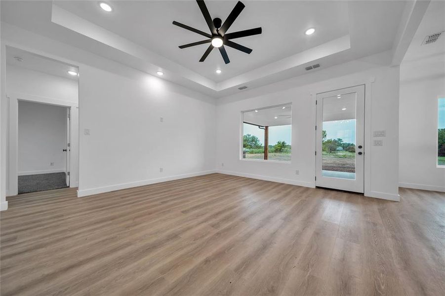 Unfurnished living room featuring ceiling fan, light hardwood / wood-style floors, and a raised ceiling