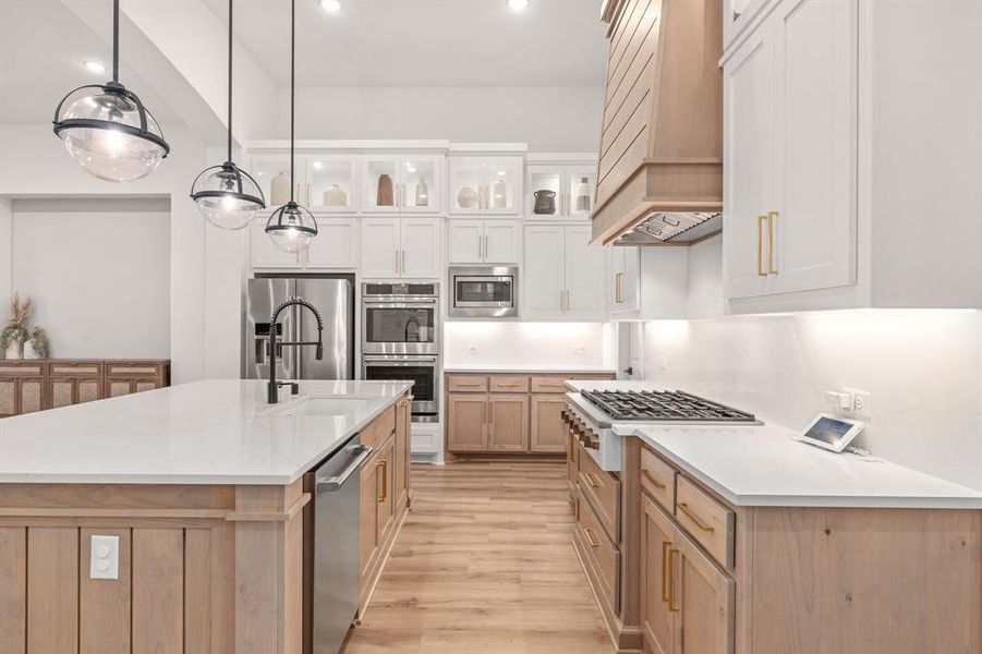 Kitchen featuring decorative light fixtures, stainless steel appliances, light wood-type flooring, a center island with sink, and custom range hood