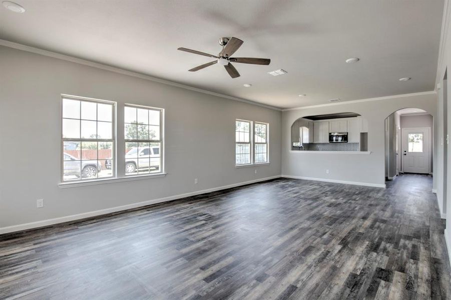 Unfurnished living room with a healthy amount of sunlight, crown molding, and dark wood-type flooring