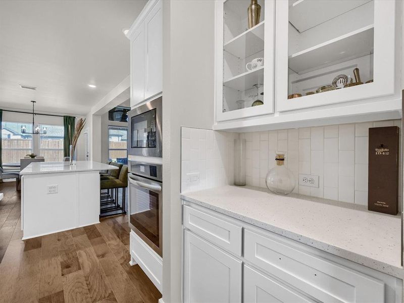 Kitchen with tasteful backsplash, light stone countertops, dark hardwood / wood-style flooring, hanging light fixtures, and white cabinetry