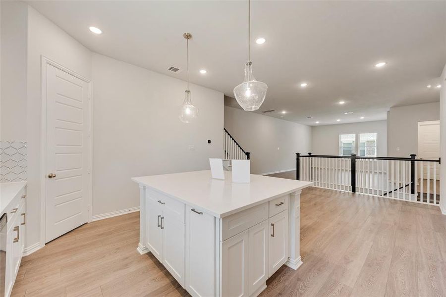 Kitchen featuring white cabinets, light hardwood / wood-style floors, a center island, and hanging light fixtures