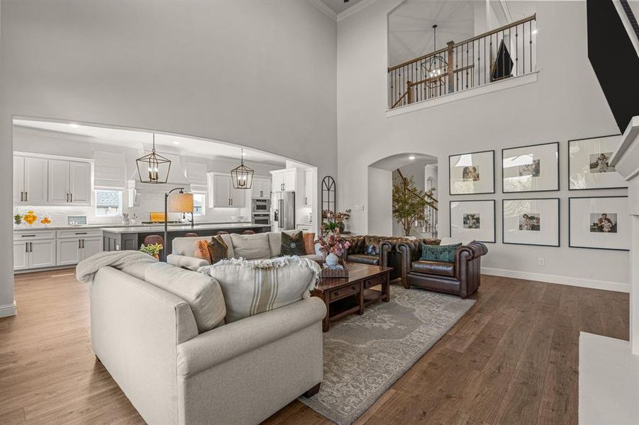 Living room featuring an inviting chandelier, ornamental molding, light hardwood / wood-style flooring, and a towering ceiling