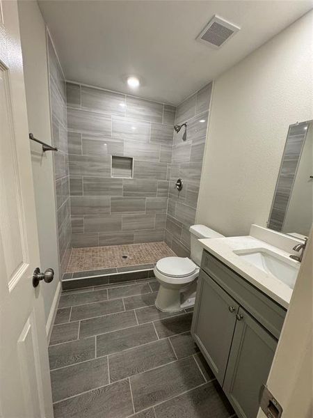 Bathroom featuring tiled shower, vanity, and toilet