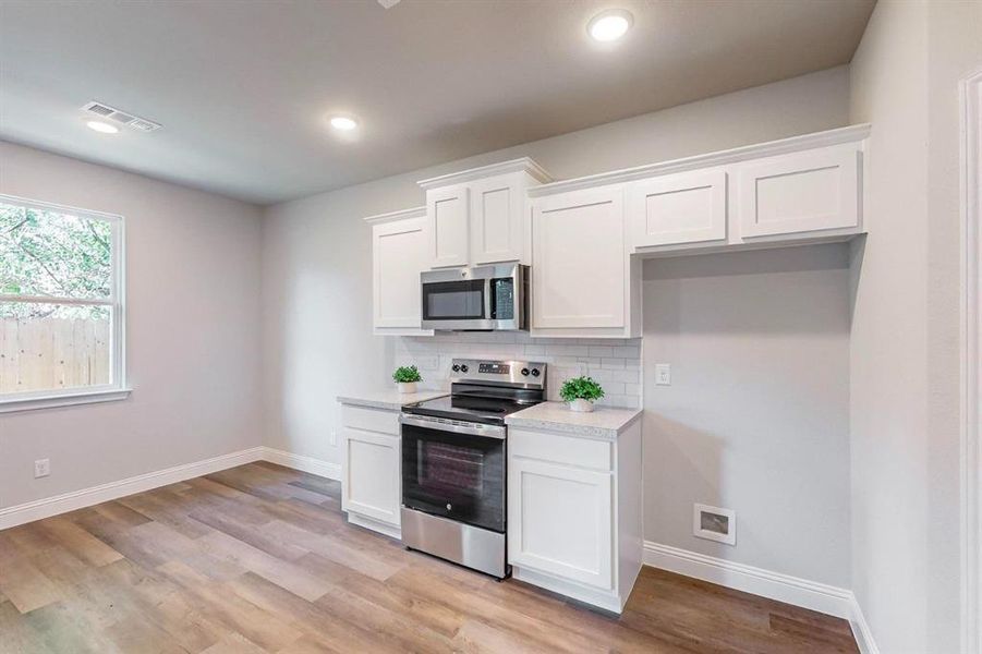 Kitchen featuring backsplash, appliances with stainless steel finishes, white cabinets, and light hardwood / wood-style floors