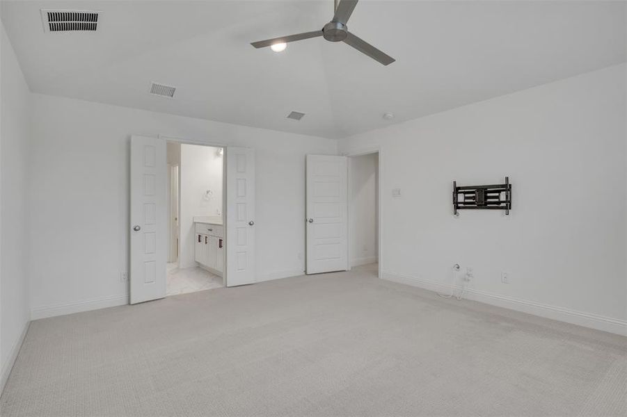 Primary bedroom featuring light colored carpet, ensuite bath, and ceiling fan