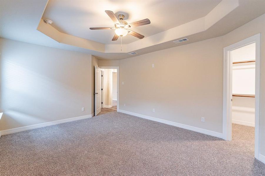 Primary bedroom featuring a tray ceiling, light colored carpet, and ceiling fan, walk in closet