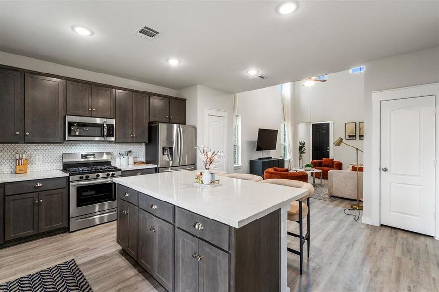 Kitchen with a kitchen breakfast bar, light hardwood / wood-style flooring, dark brown cabinets, a center island, and appliances with stainless steel finishes