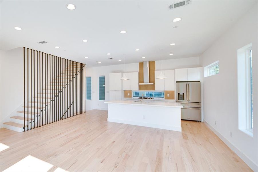 Kitchen with a kitchen island with sink, wall chimney exhaust hood, hanging light fixtures, high quality fridge, and white cabinetry