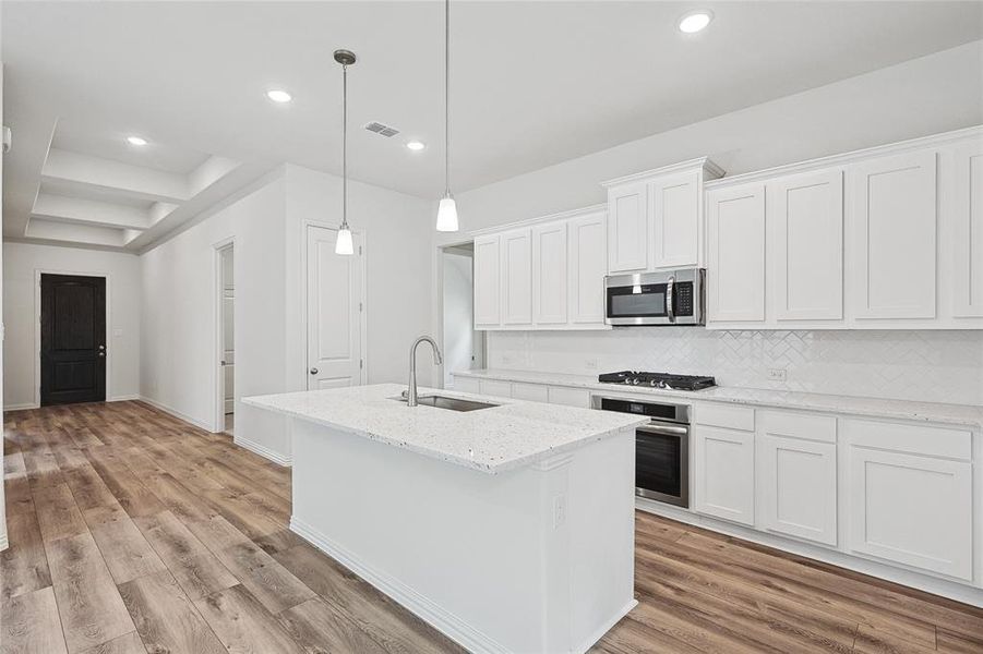 Kitchen featuring white cabinetry, stainless steel appliances, sink, light hardwood / wood-style flooring, and backsplash