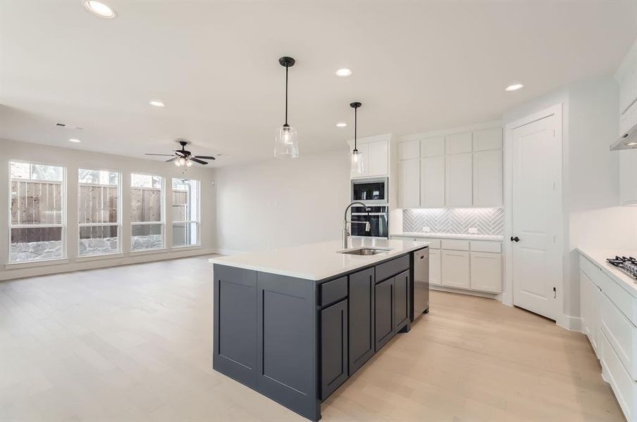 Kitchen featuring sink, white cabinetry, stainless steel appliances, decorative light fixtures, and a kitchen island with sink