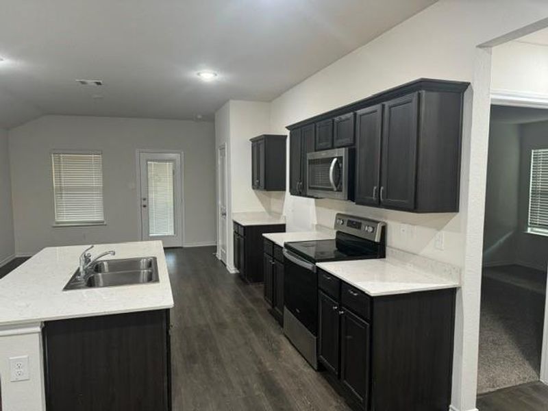 Kitchen with dark hardwood / wood-style floors, a kitchen island with sink, sink, and stainless steel appliances