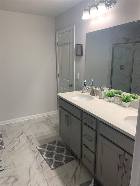 Bathroom with tiled shower, tile flooring, and double sink vanity