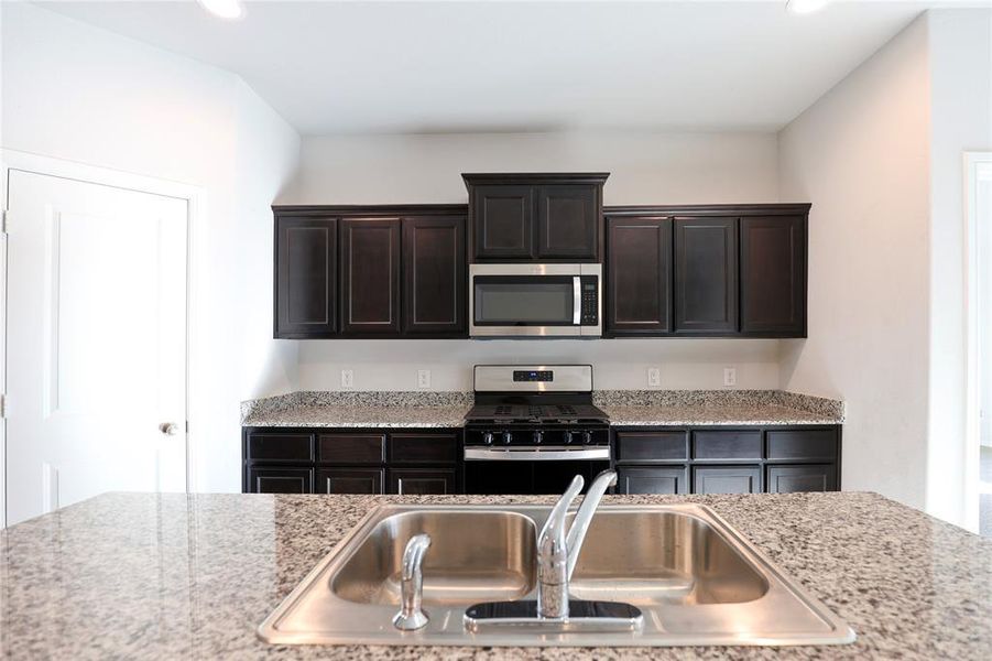 Kitchen featuring dark brown cabinetry, appliances with stainless steel finishes, sink, and light stone countertops