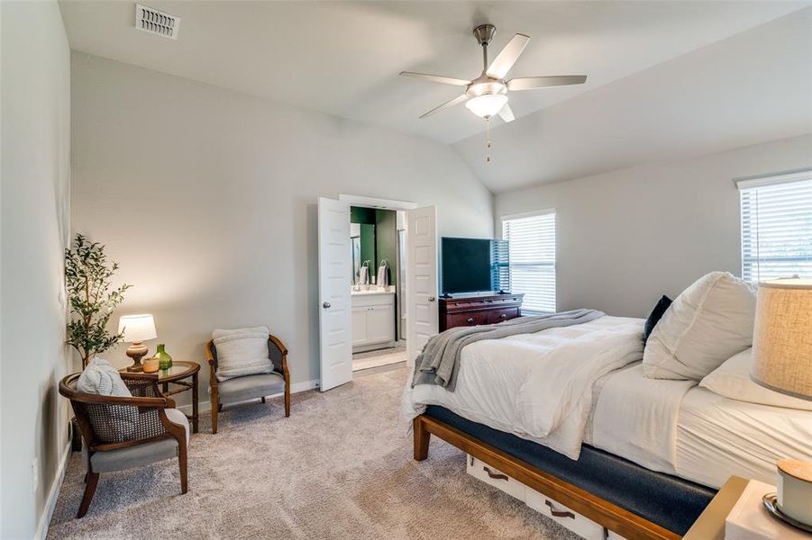 Carpeted bedroom with ceiling fan, connected bathroom, vaulted ceiling, and multiple windows