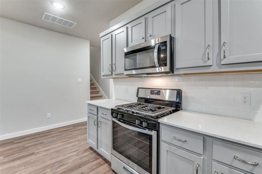 Kitchen with light hardwood / wood-style floors, gray cabinets, light stone counters, and stainless steel appliances