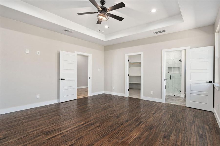 Unfurnished bedroom with dark wood-type flooring, a closet, ceiling fan, ensuite bathroom, and a walk in closet