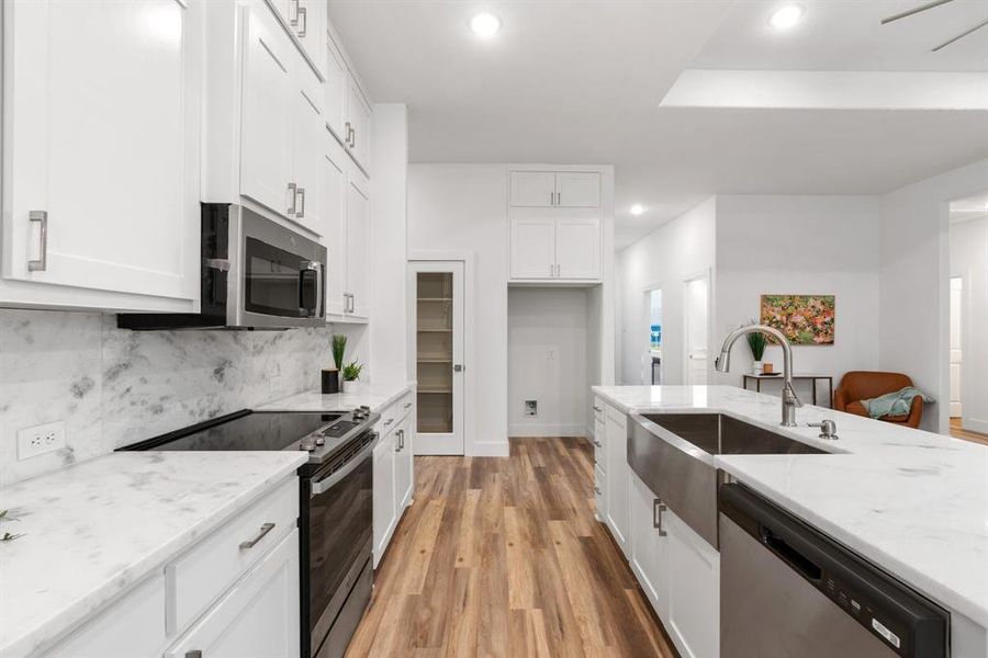 Kitchen featuring light stone countertops, stainless steel appliances, white cabinets, sink, and light hardwood / wood-style flooring