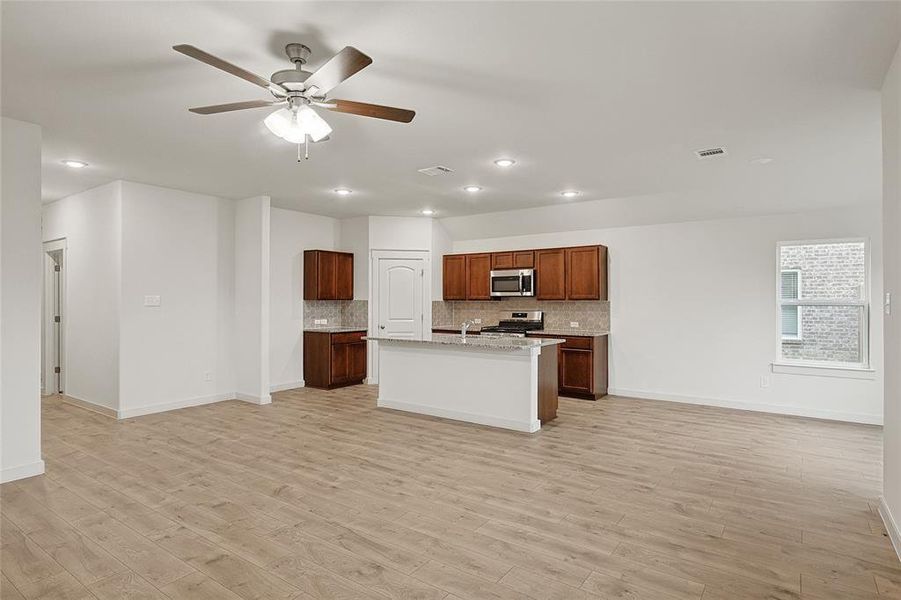 Kitchen featuring a center island with sink, backsplash, appliances with stainless steel finishes, ceiling fan, and light wood-type flooring