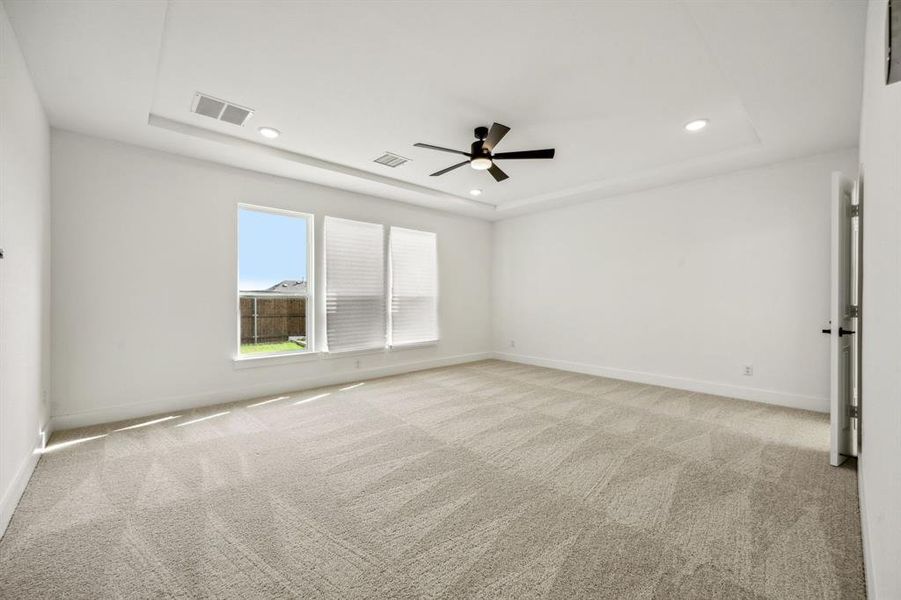 Carpeted spare room featuring a tray ceiling and ceiling fan