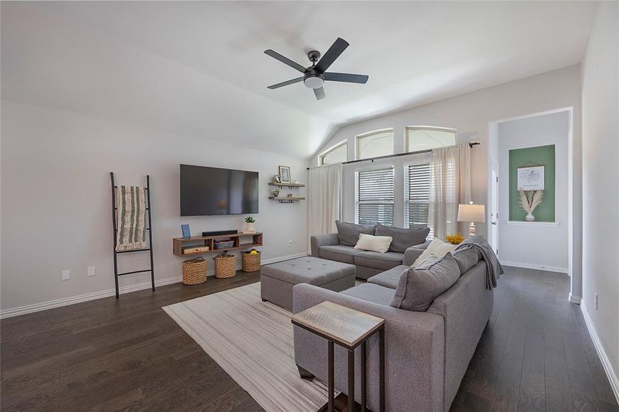 Living room with ceiling fan, vaulted ceiling, and dark wood-type flooring