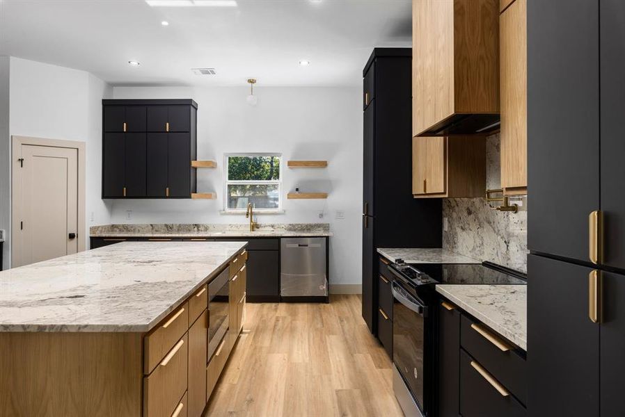 Kitchen featuring wall chimney range hood, light stone counters, light hardwood / wood-style floors, a kitchen island, and appliances with stainless steel finishes