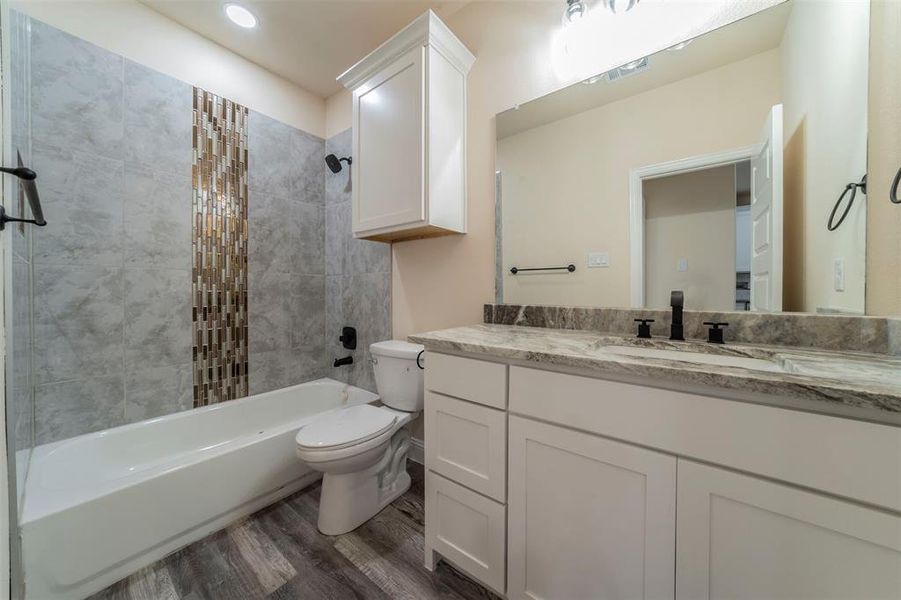 Full bathroom featuring hardwood / wood-style floors, toilet, tiled shower / bath combo, and vanity