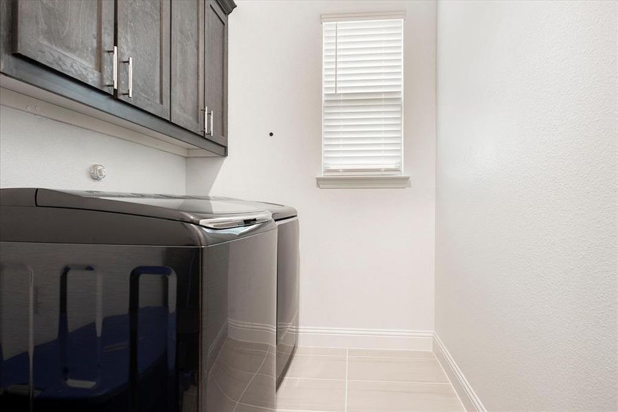 Laundry room featuring cabinets, light tile patterned floors, and washing machine and clothes dryer