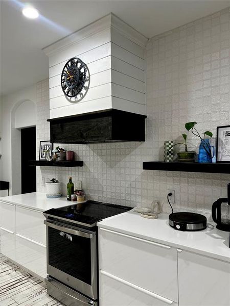 Kitchen with light tile patterned floors, backsplash, electric stove, and premium range hood