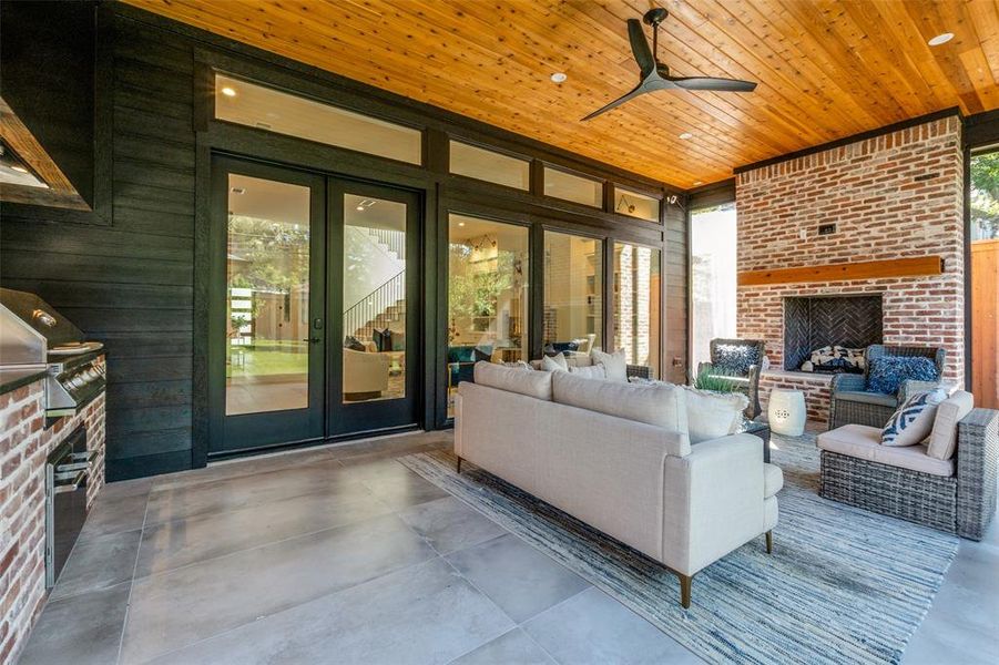 Living room with wood walls, a brick fireplace, ceiling fan, wood ceiling, and concrete flooring