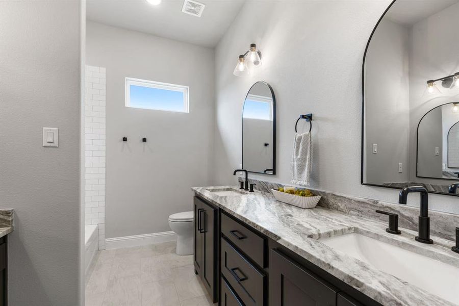 Full bathroom with tile flooring, dual vanity, washtub / shower combination, and toilet