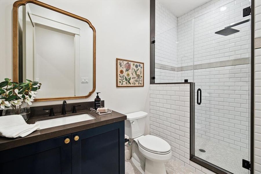 Full bathroom located on the first floor with penny tile floor, black plumbing fixtures, a glass enclosed shower with subway tiles and a tile accent band.