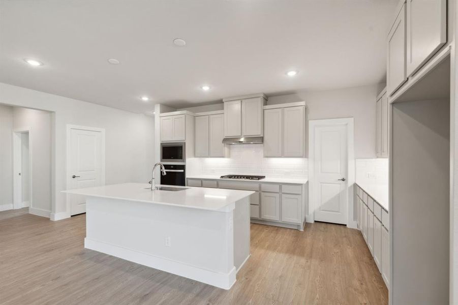 Kitchen with built in microwave, light hardwood / wood-style flooring, an island with sink, stainless steel oven, and decorative backsplash