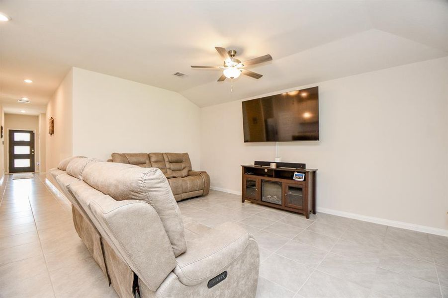 This is a spacious living room featuring tiled flooring, a neutral color palette, a ceiling fan, and large windows.  The entryway is visible, suggesting a welcoming, open layout.