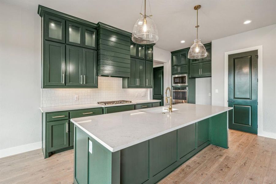 Kitchen with a center island with sink, green cabinetry, appliances with stainless steel finishes, and light hardwood / wood-style flooring