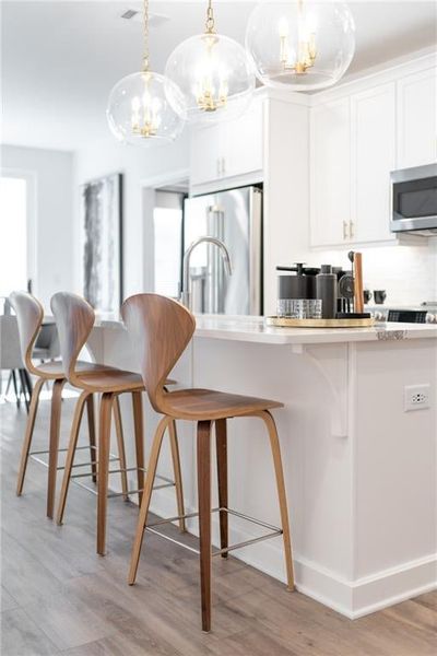 Kitchen featuring hanging light fixtures, white cabinetry, appliances with stainless steel finishes, a kitchen breakfast bar, and hardwood / wood-style floors