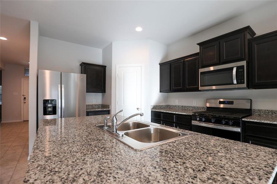 Kitchen with appliances with stainless steel finishes, sink, light stone countertops, and light tile floors