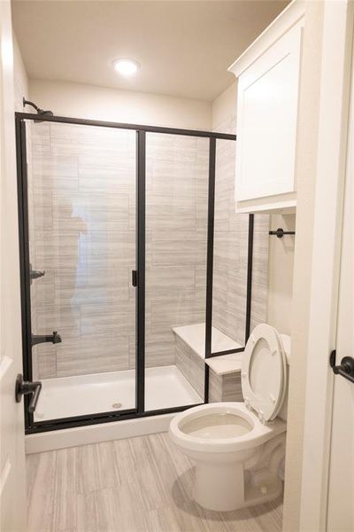 Bathroom featuring a shower with shower door, toilet, and tile patterned flooring