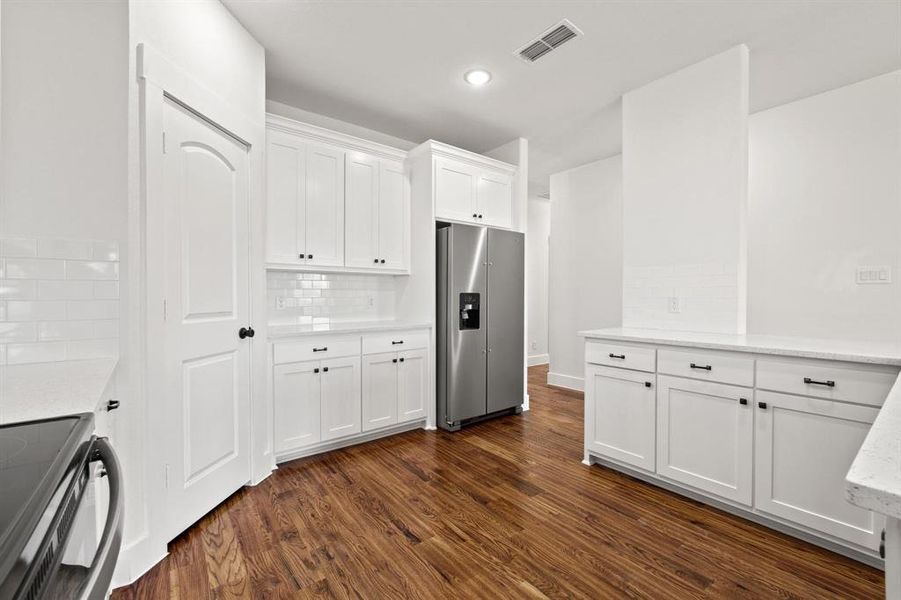 Kitchen featuring dark wood-type flooring, range, white cabinets, stainless steel refrigerator with ice dispenser, and backsplash