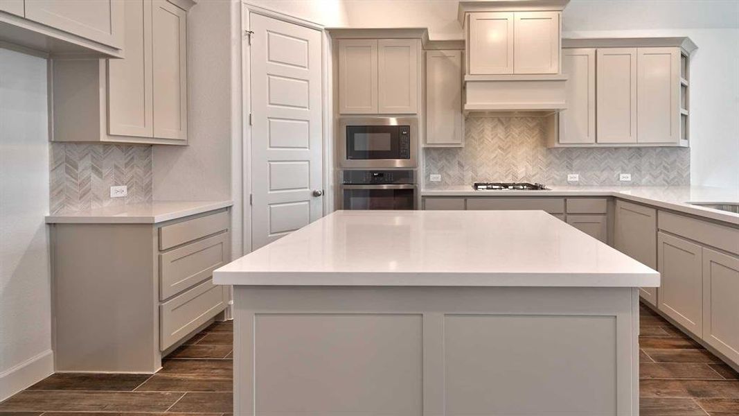 Kitchen featuring gray cabinets, decorative backsplash, oven, a kitchen island, and black microwave