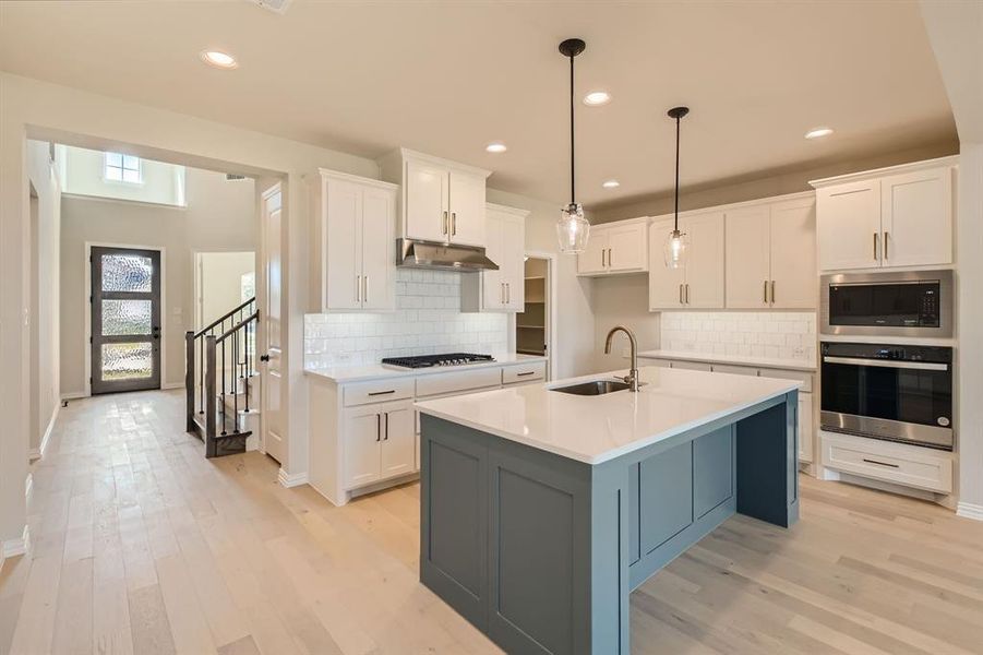 Kitchen featuring white cabinets, a center island with sink, sink, decorative light fixtures, and stainless steel appliances