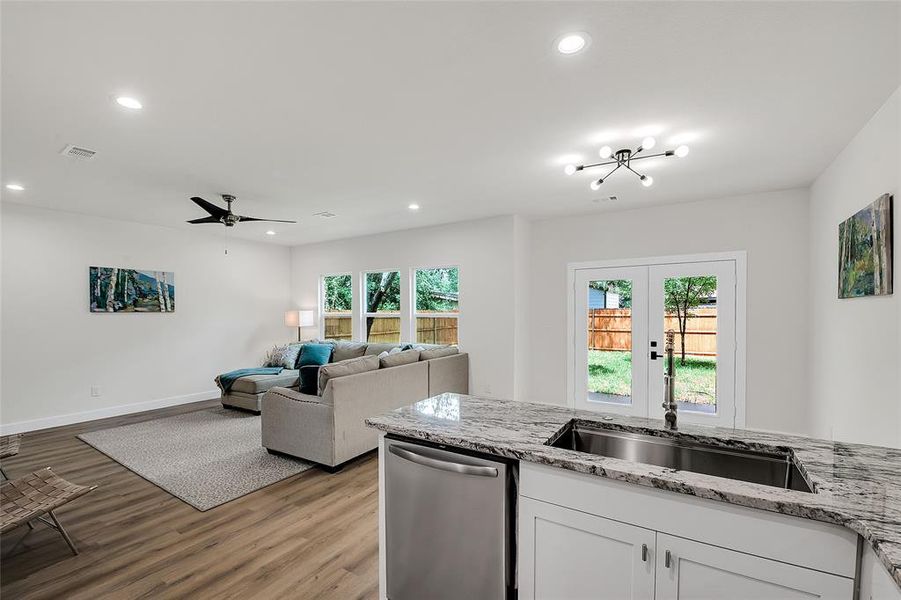 Kitchen featuring plenty of natural light, light granite countertops, wood-style flooring, and white custom cabinetry