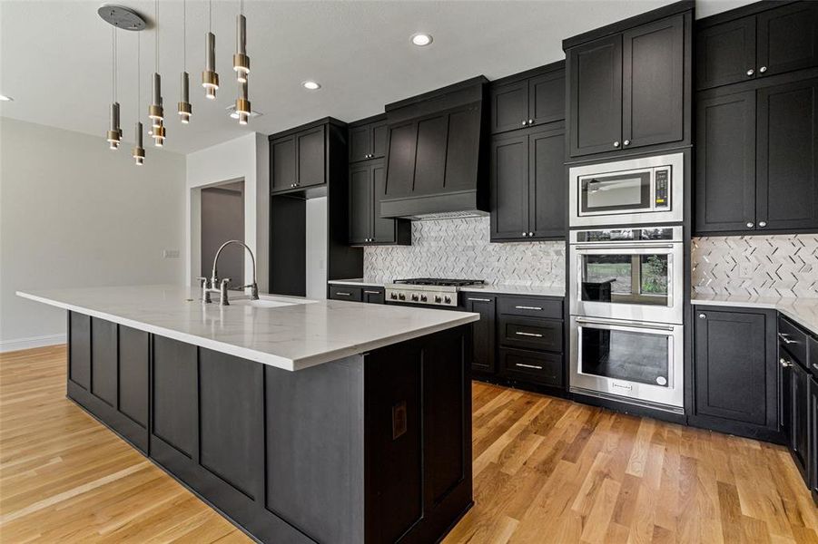 Kitchen featuring light hardwood / wood-style floors, sink, an island with sink, and hanging light fixtures